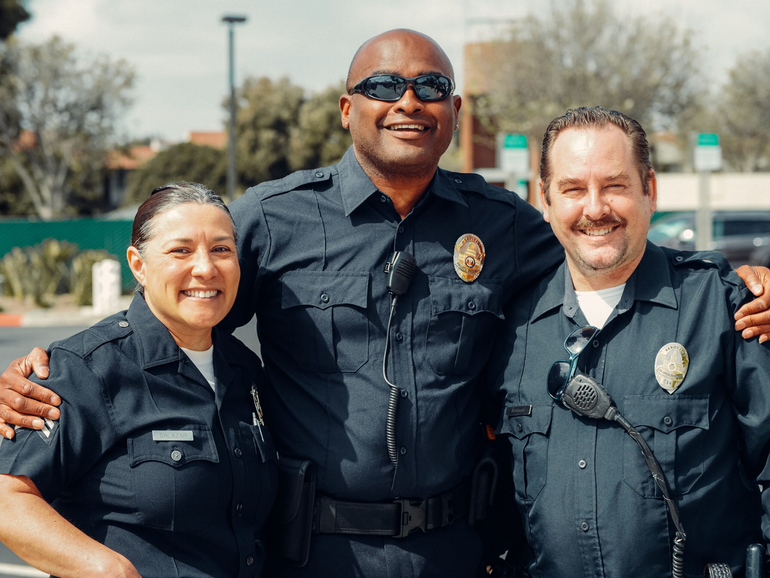 Home Three police officers smiling and posing in an outdoor setting, showcasing camaraderie in law enforcement.
